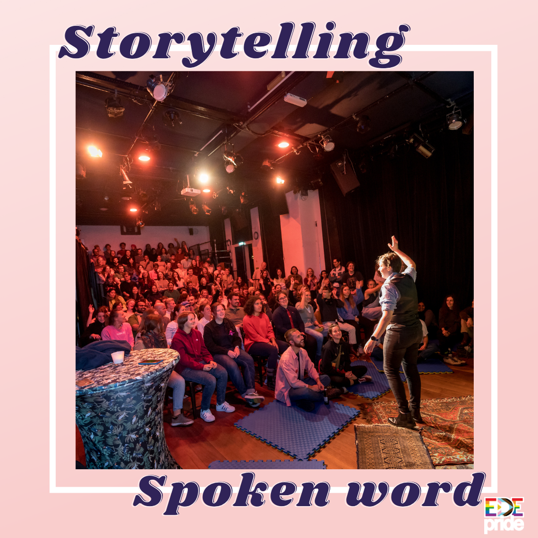 een foto van iemand met kort haar, een spijkerbroek en een blouse aan, die in een zaal tegenover een grote groep mensen staat en diens rechterhand in de lucht steekt. De mensen in de zaal lachen en sommigen steken ook hun hand in de lucht. In paarse letters staat bovenaan 'storytelling' en onderaan 'spoken word'.